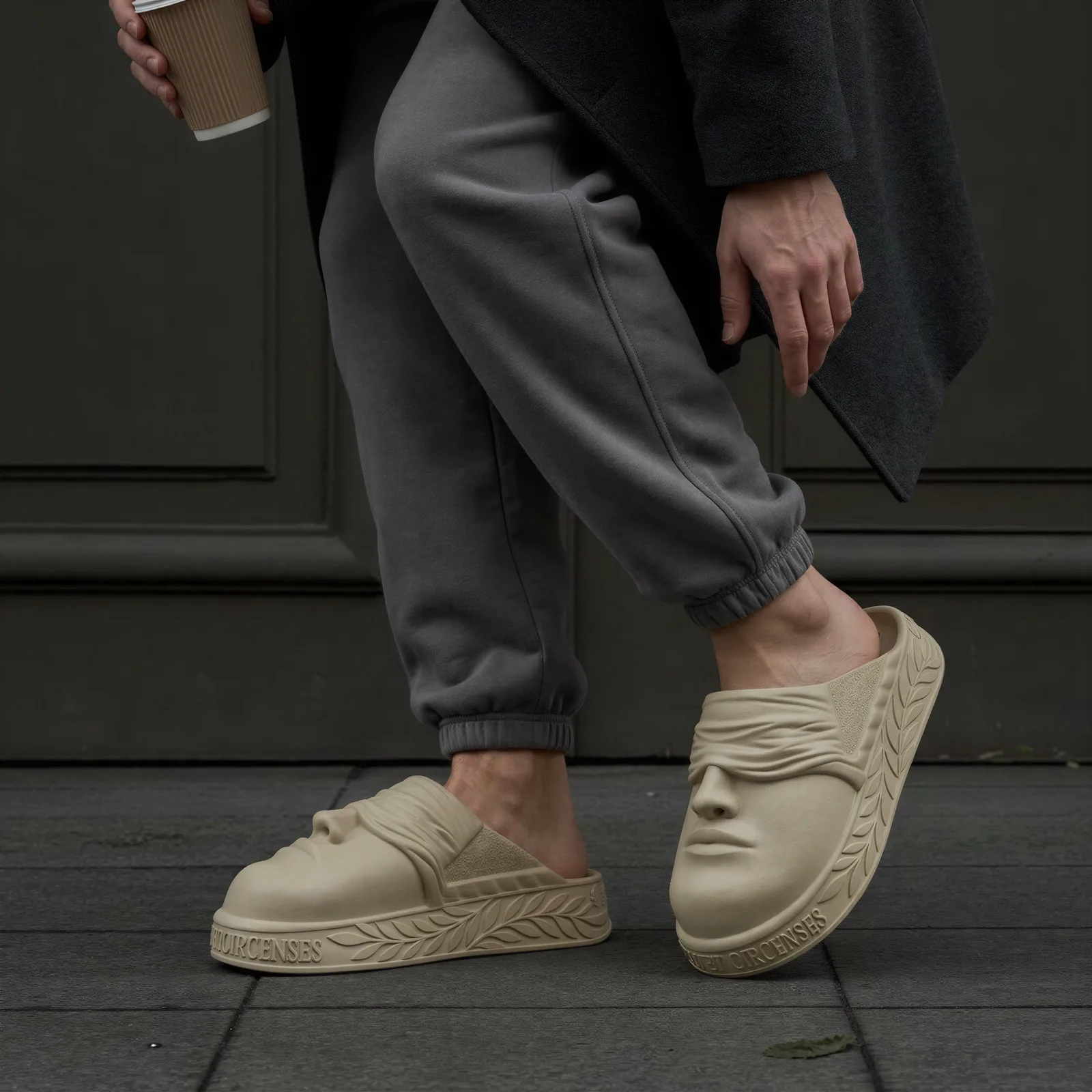 On foot: the BLINDED mules worn with grey sweatpants and a long coat, coffee in hand